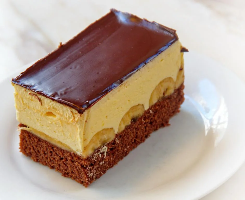 Eine Bananenschnitte mit heller Creme und einer glänzenden Schokoladenglasur