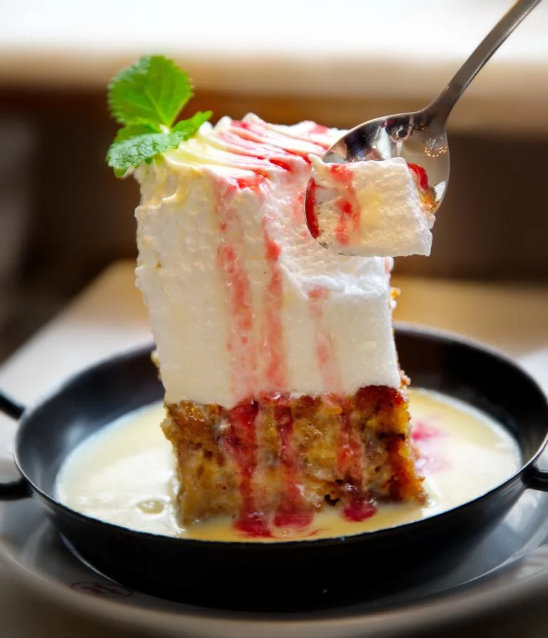 Ein Stück Torte mit heller Creme und roten Fruchtschichten auf einem kleinen Teller